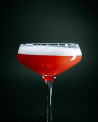 Red cocktail in a martini glass against a black background