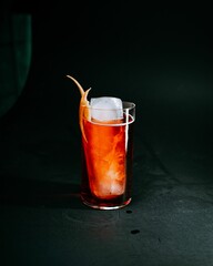 Poster - Glass containing red colored cocktail and ice on a dark surface