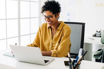 graphic designer smiles as she works on a laptop in an office