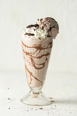 Wall Mural - Glass of freshly prepared chocolate milkshake on a white table, with chocolate flakes on top