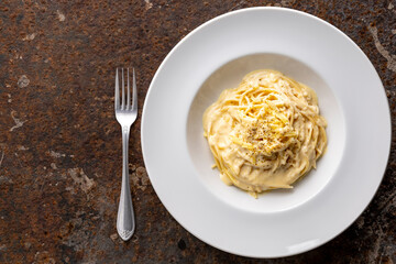 Wall Mural - spaghetti carbonara with cream sauce in classy white circle ceramic plate beside fork on rusty texture background with copy space for text, top view, flat lay