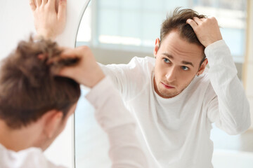 Wall Mural - Young man with hair loss problem looking in mirror at home