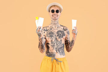 Wall Mural - Tattooed man with sunscreen creams on beige background