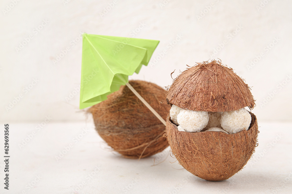 Coconut shell with white chocolate candies and green umbrella on light table