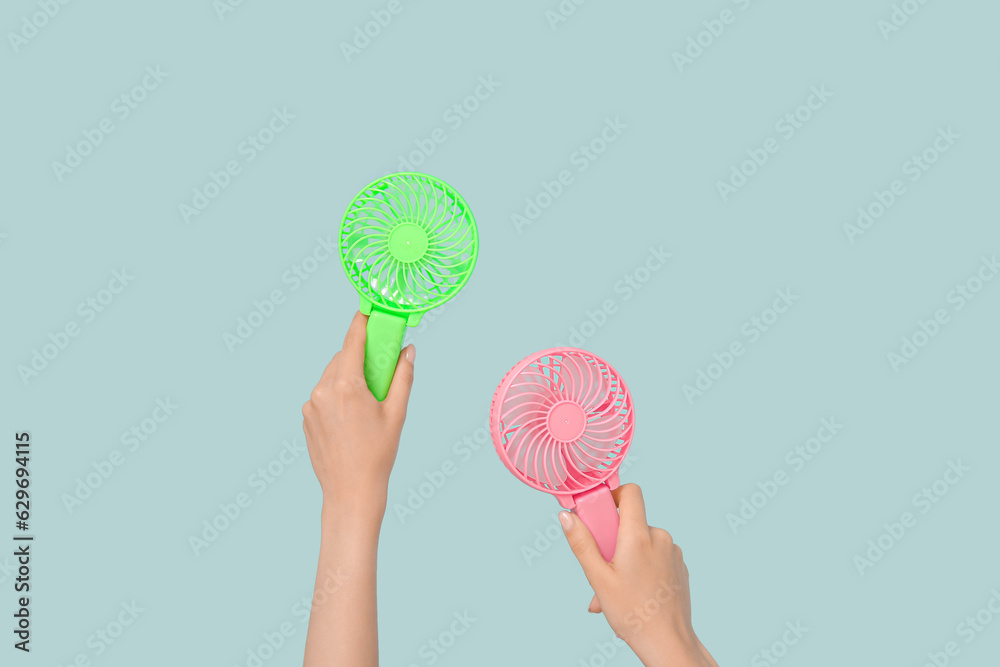 Female hands with mini fans on blue background