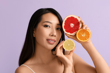 Sticker - Beautiful young Asian woman with citrus fruits on lilac background