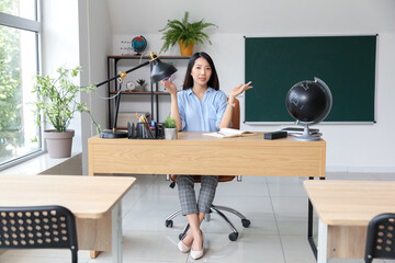 Canvas Print - Female Asian teacher sitting at table in classroom