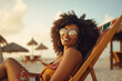 Joyful black woman, in fashion sunglasses, rests on a tropical beach chair, wearing glasses, enjoying vacation