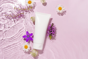 White mockup of a tube of cream or lotion on a pink background with water waves and flowers. Salon facial care, beauty, spa, moisturizing and rejuvenation concept.