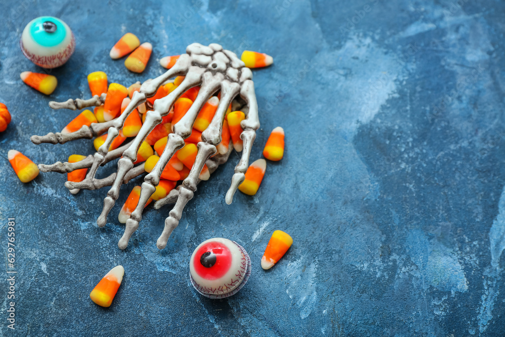 Tasty Halloween candy corns, skeleton and eyes on blue background, closeup