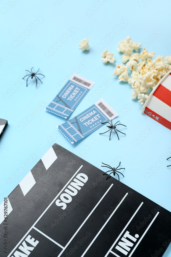 Tasty popcorn, clapperboard and cinema tickets on blue background, closeup. Halloween celebration