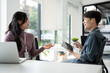© bongkarn - A happy Asian male office worker enjoys discussing work with a female colleague in the office