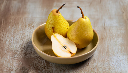 Poster - Two whole yellow pears and one half in a beige bowl on rustic background