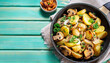Fried potatoes with mushrooms, onions and parsley served in a frying pan with turquoise wooden background