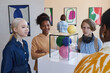 © Seventyfour - Diverse group of smiling teenagers listening to female teacher or tour guide in modern art gallery