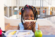 Happy african american schoolgirl having healthy lunch eating sandwich at elementary school