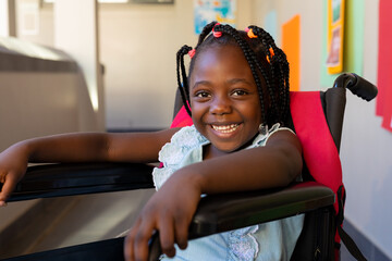 Portrait of happy african american schoolgirl sitting in wheelchair at elementary school corridor