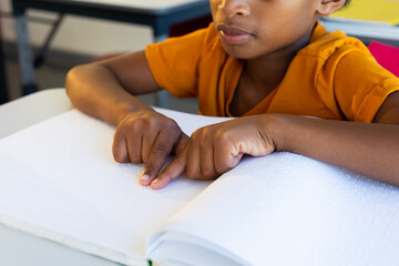 Focused biracial schoolboy reading braille with hands in classroom