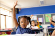 Diverse elementary schoolchildren sitting at desks and raising hands in class