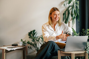 Wall Mural - Smiling businesswoman talking with client via video call and showing thumb up sitting in coworking