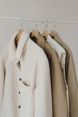 Wall Mural - Autumn outerwear on hanger over white wall. Warm jackets, coats. Aesthetic wardrobe with clothes in neutral colours