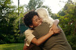 © pressmaster - Happy African American boy giving hug to his grandfather with long white hair while expressing gladness during meeting in natural environment