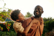 © pressmaster - Happy cute African American boy embracing his father behind back and having fun with him in front of camera in the garden with green trees