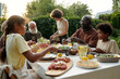 © pressmaster - Modern family of siblings, their intercultural parents and grandparents sitting by dinner table served with homemade food and drinks