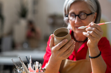 Woman enjoying creative process of pottery coloring in pottery workshop.