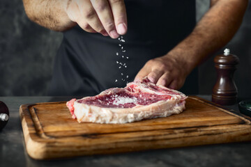Poster - Man cook sprinkles salt on a fresh raw beef steak on the bone