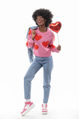 Happy black woman with afro hair and denim outfit is holding ballon heart on isolated white background.