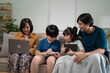 © NINENII - Happy parents with two kids using smartphone at home together, sitting on couch, smiling mother and father with little son and daughter looking at phone screen, having fun
