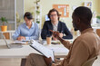 © Seventyfour - Side view portrait of black young man holding clipboard while leading business meeting with team in office and discussing project strategy, copy space