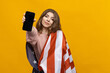 © makedonski2015 - A young woman with an American flag on her shoulders holds a mobile phone on a yellow background. The ability to place ads on a smartphone. Mockup