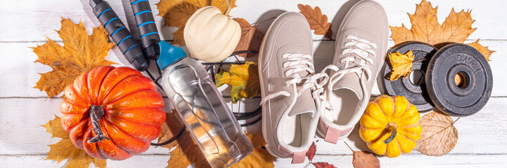 Autumn sport fitness background. Outdoors fall workouts concept. Running sneakers, dumbbell barbell discs, jump rope, water bottle, wooden background, with autumn leaves, pumpkins top view copy space