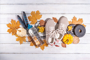 Autumn sport fitness background. Outdoors fall workouts concept. Running sneakers, dumbbell barbell discs, jump rope, water bottle, wooden background, with autumn leaves, pumpkins top view copy space