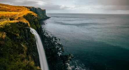 Wall Mural - Majestic waterfall cascading down a grassy hillside, located near the shore of a tranquil ocean