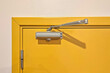 Door closer for entrance door. Automatic hydraulic device, leaver hinge door closer holder, Yellow door.