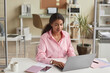 © Seventyfour - Portrait of black young woman wearing pink in office while using computer, copy space