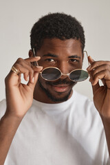 Wall Mural - Vertical portrait of smiling black man looking over sunglasses in white studio