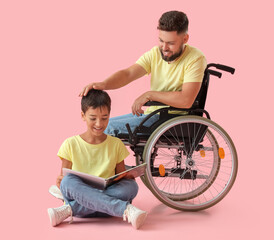 Poster - Little boy and his father in wheelchair reading book on pink background