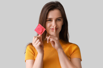 Wall Mural - Young woman with condom showing silence gesture on light background, closeup