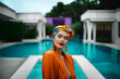 © ADDICTIVE STOCK - Generative AI image of positive eclectic female with an orange shirt near swimming pool looking at camera with a headscarf