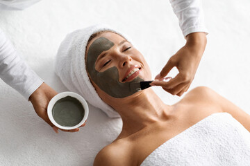 Wall Mural - Aesthetic Procedure. Beautician Applying Clay Face Mask On Middle Aged Woman Face