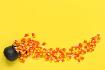 Wall Mural - Cauldron with tasty Halloween candy corns on yellow background