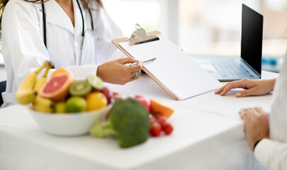 European middle aged woman doctor nutritionist in white coat show diet program to lady patient in clinic interior