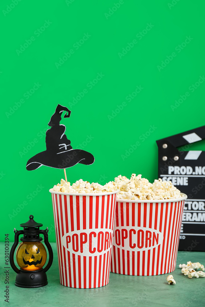 Buckets with tasty popcorn, lantern and clapperboard on green background. Halloween celebration