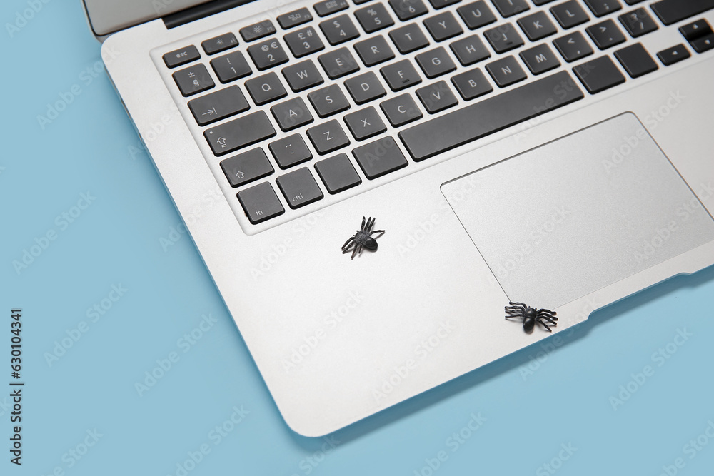 Modern laptop and spiders for Halloween on blue background, closeup