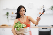Close Up Of Adult In Terracotta Tank Top Taking Self-picture Via Smartphone Boom Arm While Carrying Groceries In Bag. Beautiful Lady Encouraging To Healthy Well-being Via Eating Habits And Training.