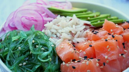 Poster - Poke bowl with salmon, rice, avocado, wakame salad, onion, circling on table. Healthy food, Asian raw meal. traditional Hawaiian raw fish salad. Japanese food.